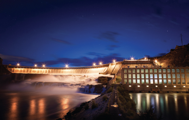Hydroelectric dam generating electricity at night with illuminated powerhouse and flowing water.